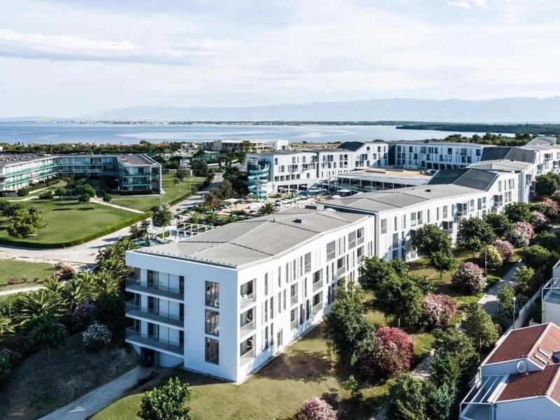 Moderní hotelový komplex s několika bílými budovami a výhledem na moře v dálce.