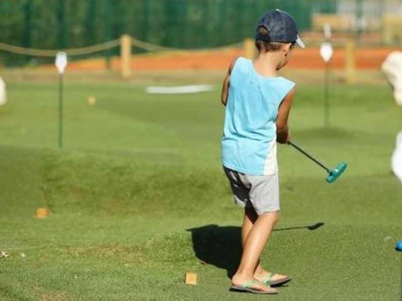 Dítě hraje minigolf na slunném, zeleném hřišti s klobouky a míčky.