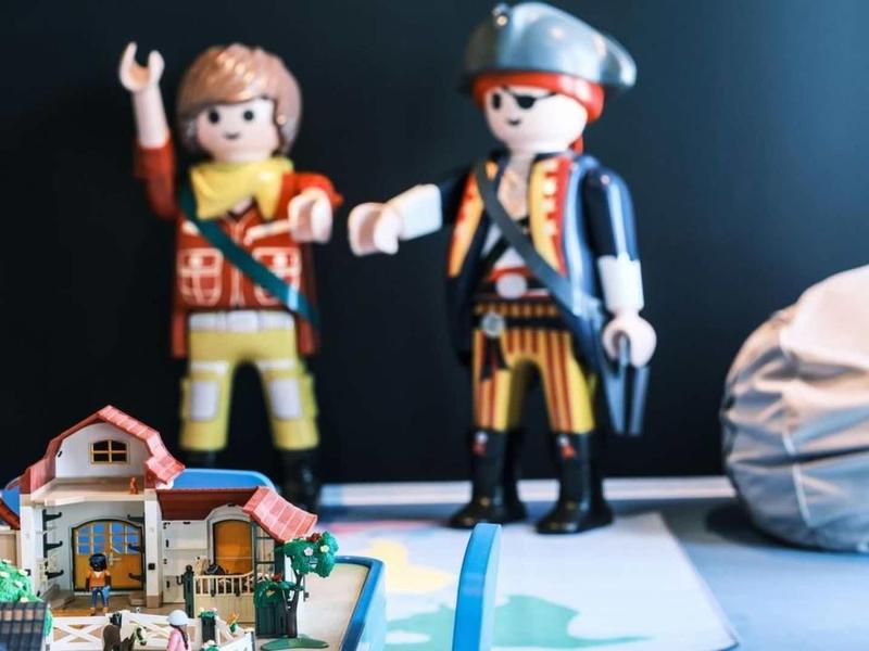 Dvě hračka postavy, včetně piráta a kovboje, stojí před malými domy a předměty.