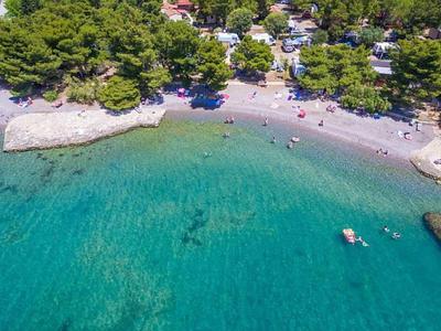 Clear turquoise water by a wooded beach with people and small boats.