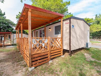 Modular wooden holiday home with covered porch in a green holiday park.