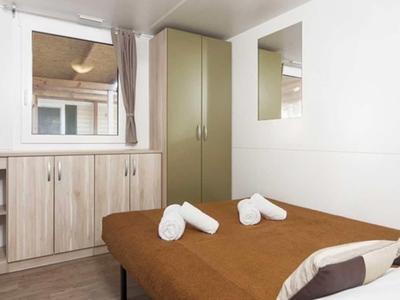 Kleine slaapkamer met twee bedden, bruine dekens, kast en raam met gordijn.