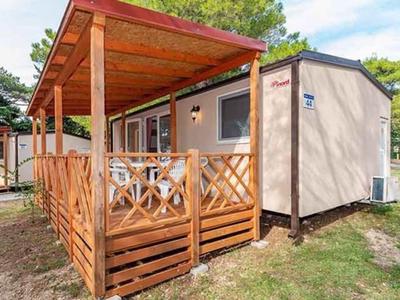 Houten huisje met overdekt terras in een bebost campinggebied bij daglicht.
