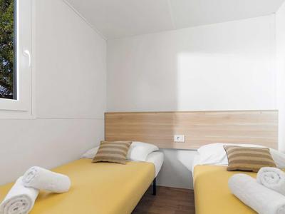 Licht hotelkamer met twee eenpersoonsbedden, houten hoofdeinde en een raam met uitzicht op een boom.
