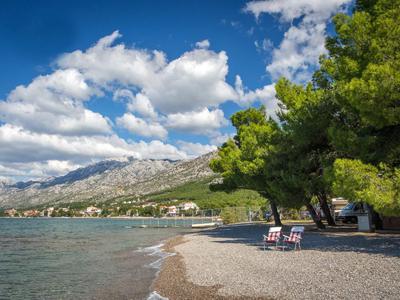 Pebble beach with two chairs and mountain view under a blue sky with clouds.