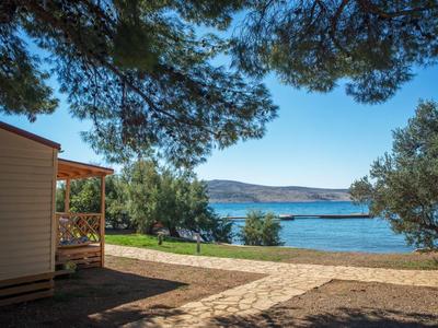 Mobile home with porch under trees by a pebble beach with sea view under clear sky.