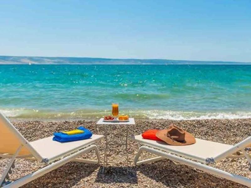 Two lounge chairs with towels and drinks on a rocky beach on a clear day