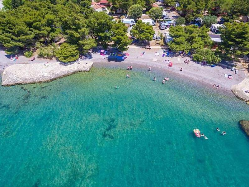 Clear turquoise water by a wooded beach with people and small boats.
