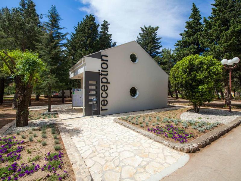 Small white reception hut surrounded by trees and flower beds in a park.