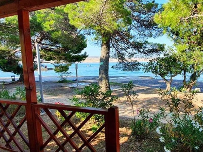 View from a porch with wooden lattice overlooking a beach with trees and the sea in the background.