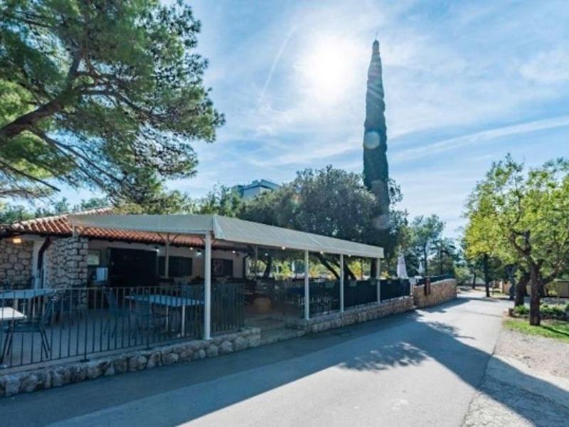 Sidewalk beside an open building with trees and church tower in the background on a clear day.