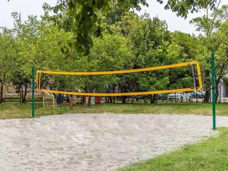 Outdoor sand volleyball court with net, surrounded by trees and grass