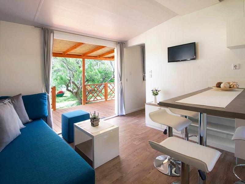 Bright hotel room with blue sofa, table, kitchenette, and view of terrace and garden.