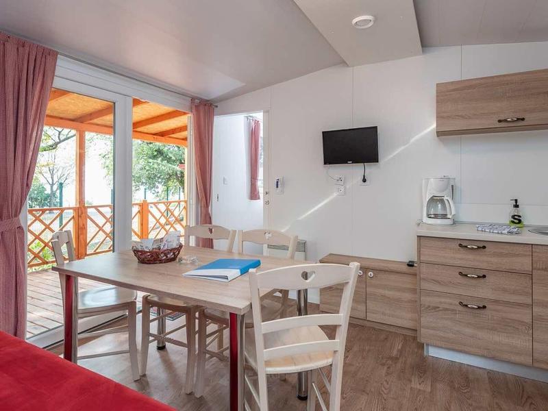 Modern kitchenette in holiday apartment with wooden cabinets, red sofa, and balcony with sunshade.