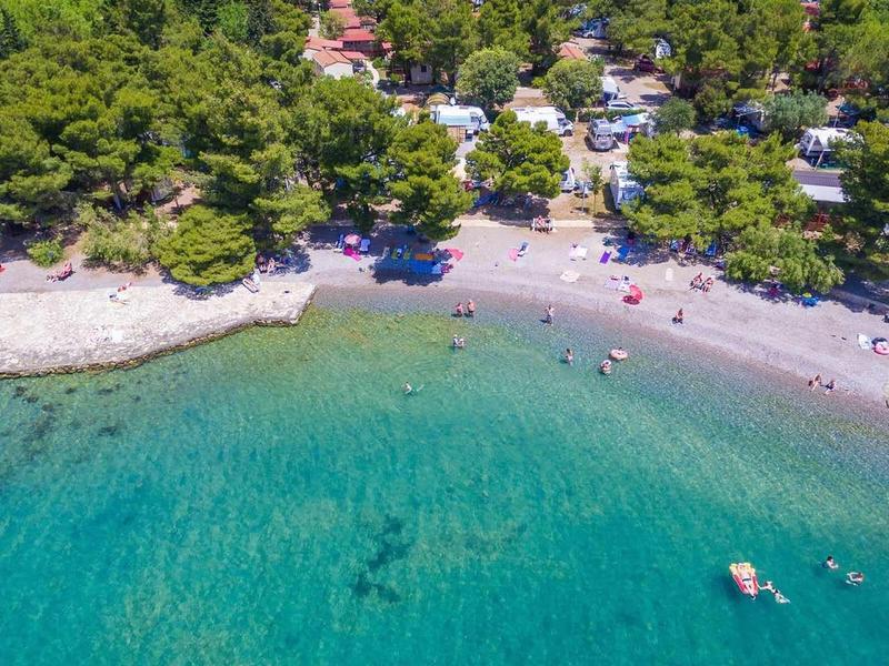Clear turquoise water and sandy beach with green trees in the background.