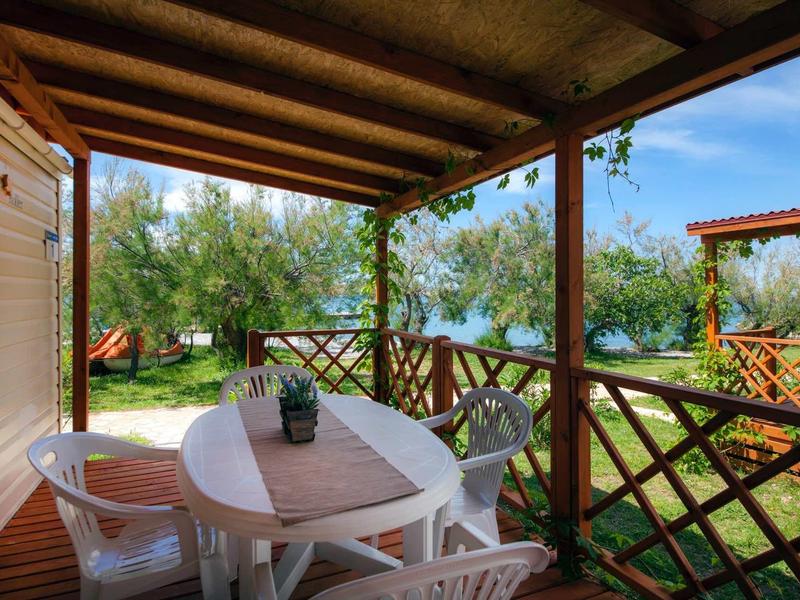 Covered terrace with white garden table and chairs, overlooking green garden and blue sky.