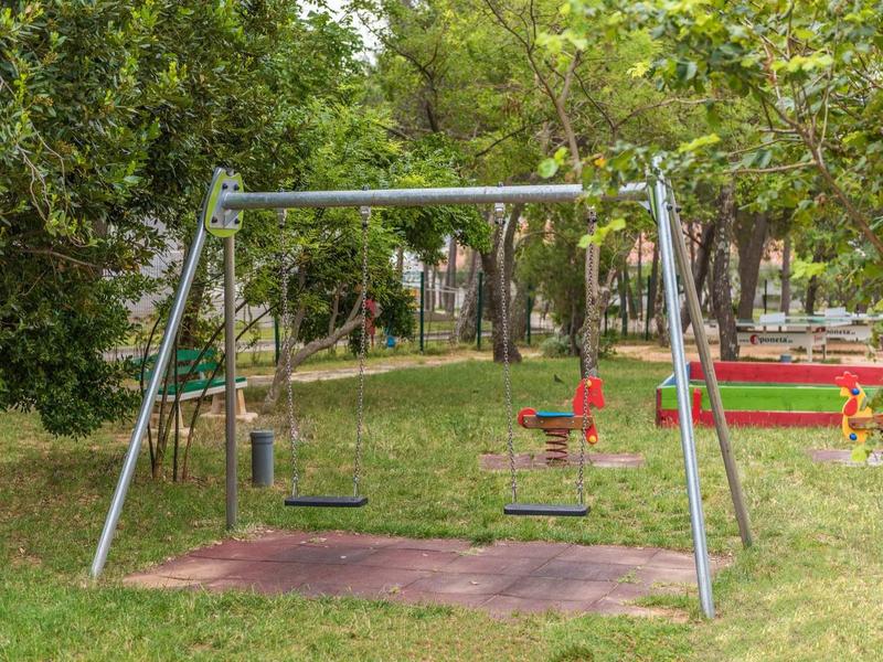 Children’s swing set with low seat and small orange spring rider on grassy park area.
