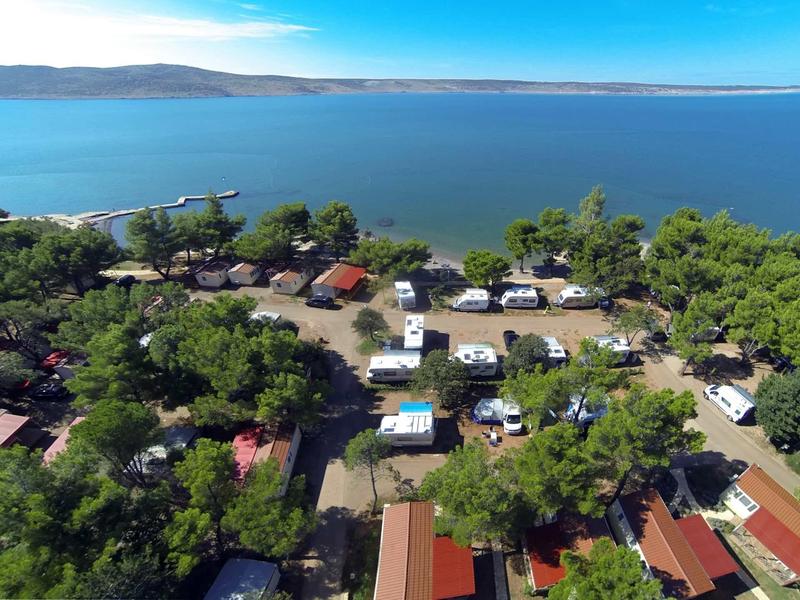 Aerial view of a campsite with motorhomes and tents beside a large lake.