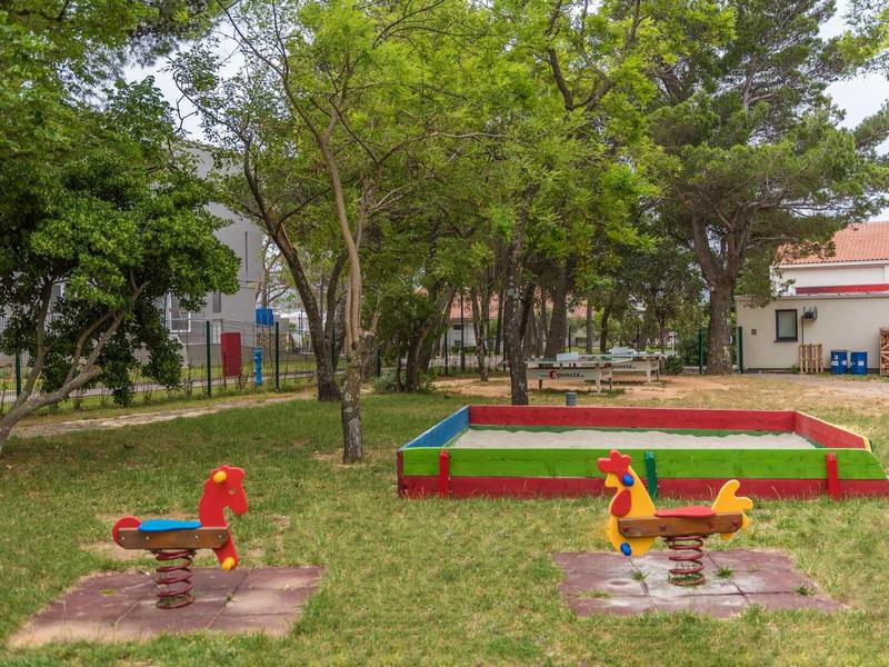 Playground with colorful spring riders and sandbox surrounded by trees and grass.