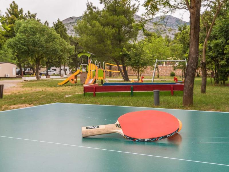 Table tennis paddles on an outdoor ping pong table with playground visible in the background.