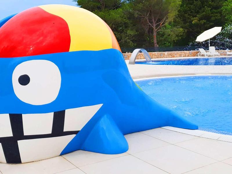 Colorful whale-shaped children's slide by a pool in a vacation setting.