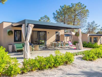 Bungalow moderne avec terrasse, rideau et jardin dans une station de vacances ensoleillée.