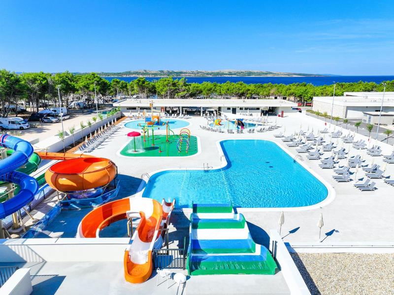 Grande piscine extérieure avec toboggans aquatiques, transats et arbres verts en arrière-plan.