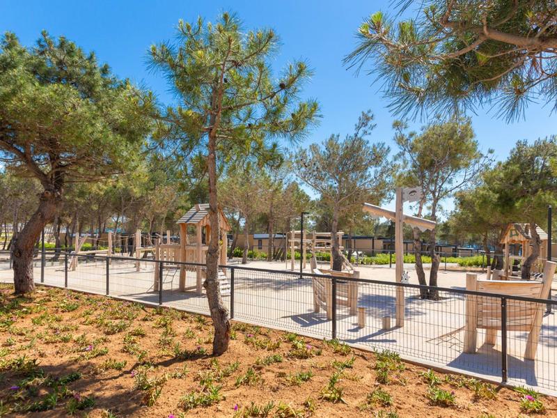 Camping ensoleillé avec des arbres, caravanes et emplacements clôturés sous un ciel bleu.