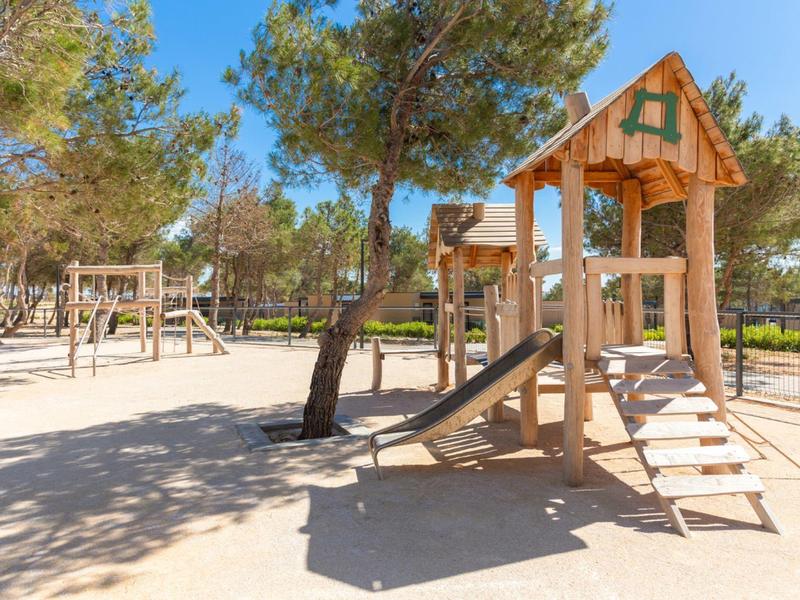 Aire de jeux pour enfants avec structure d'escalade et toboggan dans un parc ensoleillé avec des arbres.
