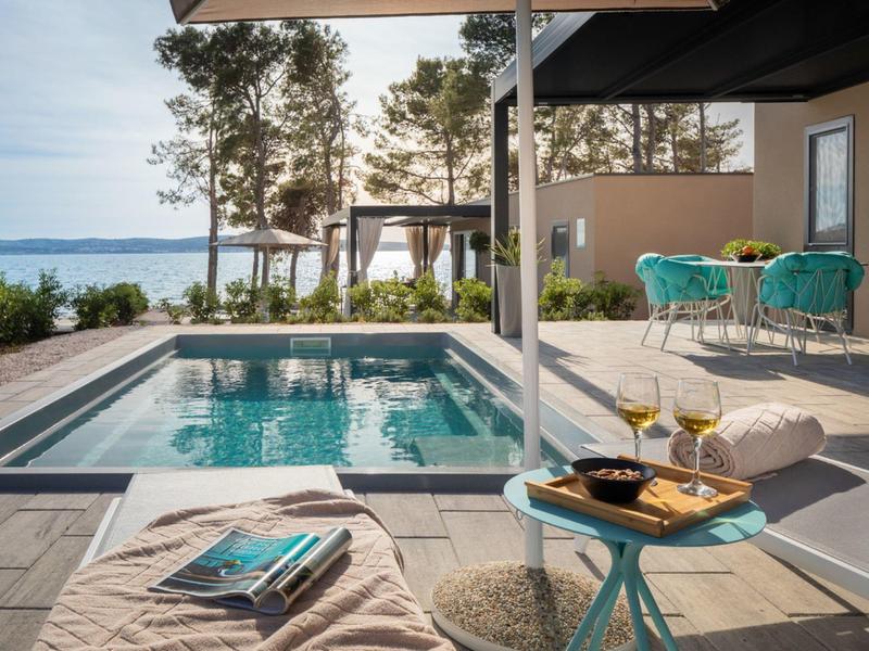 Espace piscine moderne avec transats, boissons et vue sur la mer dans un hôtel.
