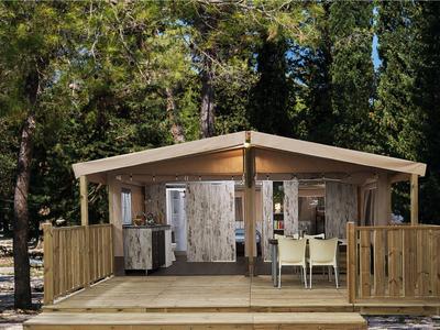 Kleines Holzhaus mit Veranda, Stühlen und Tischen, umgeben von Bäumen im Wald.