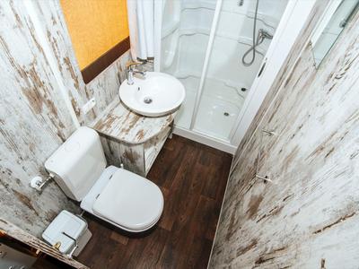 Pequeño baño con inodoro, lavabo y ducha en tonos rústicos claros.