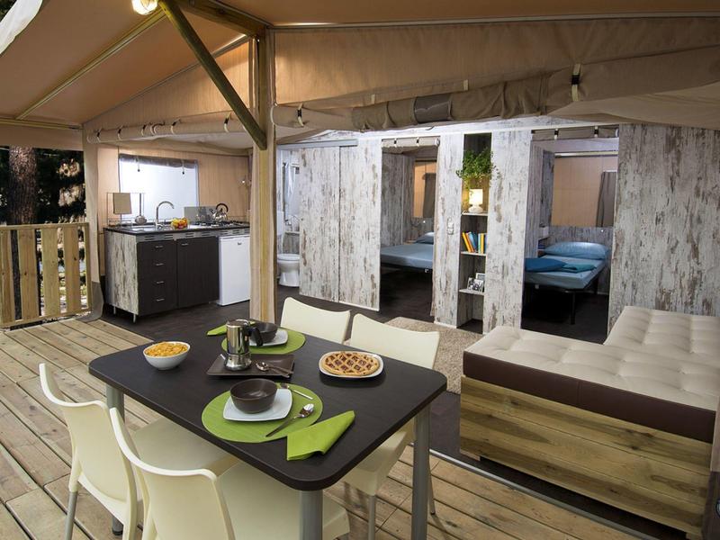 Przytulna przestrzeń na zewnątrz z stołem do jedzenia, niszą do spania i aneksem kuchennym na drewnianym tarasie.