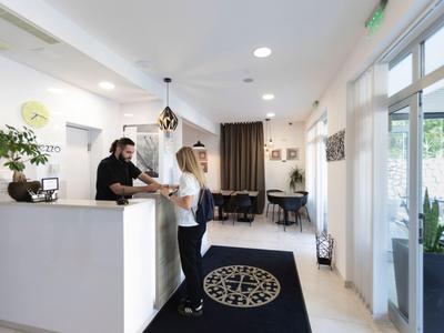 Empfangsbereich eines Hotels mit einem Mitarbeiter hinter dem Tresen und einer stehenden Gästin.