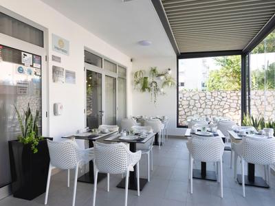 Ristorante moderno coperto con sedie bianche, tavoli, grandi finestre e piante.