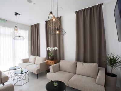Bright modern living room with gray curtains, beige sofas, and hanging light bulbs.