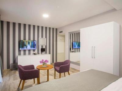 Modern hotel room with striped wall, two purple chairs, and small wooden table.