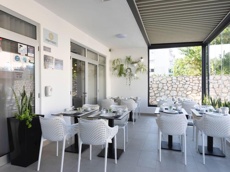Modern outdoor hotel area with white chairs and set tables under a covered space.