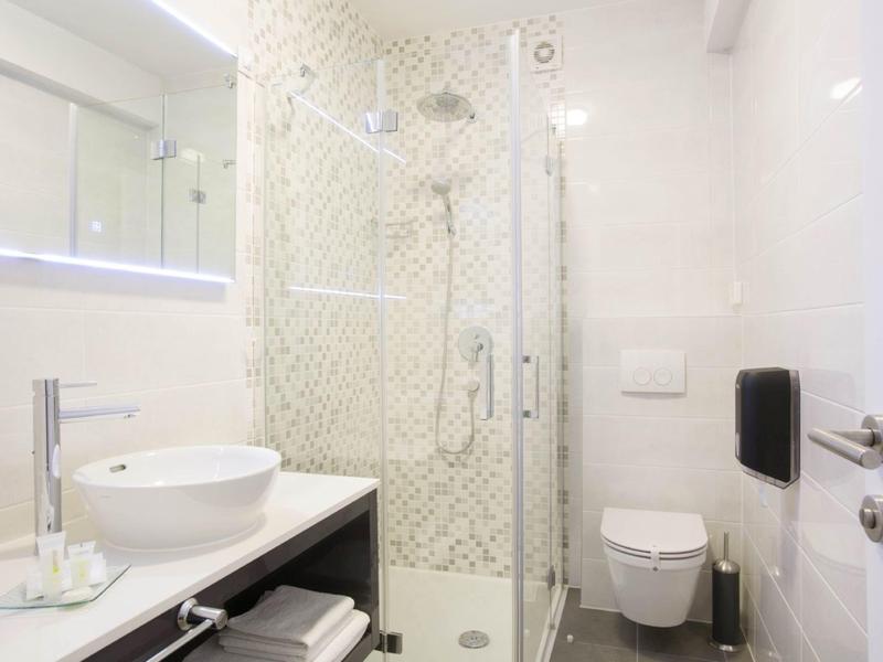 Bright, modern bathroom with glass shower, round sink, and white toilet.