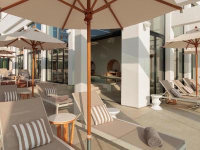 Terrasse d'hôtel ensoleillée avec chaises longues, parasols et espaces de détente confortables.