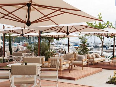 Terrasse avec des chaises confortables et des parasols avec vue sur des yachts dans le port