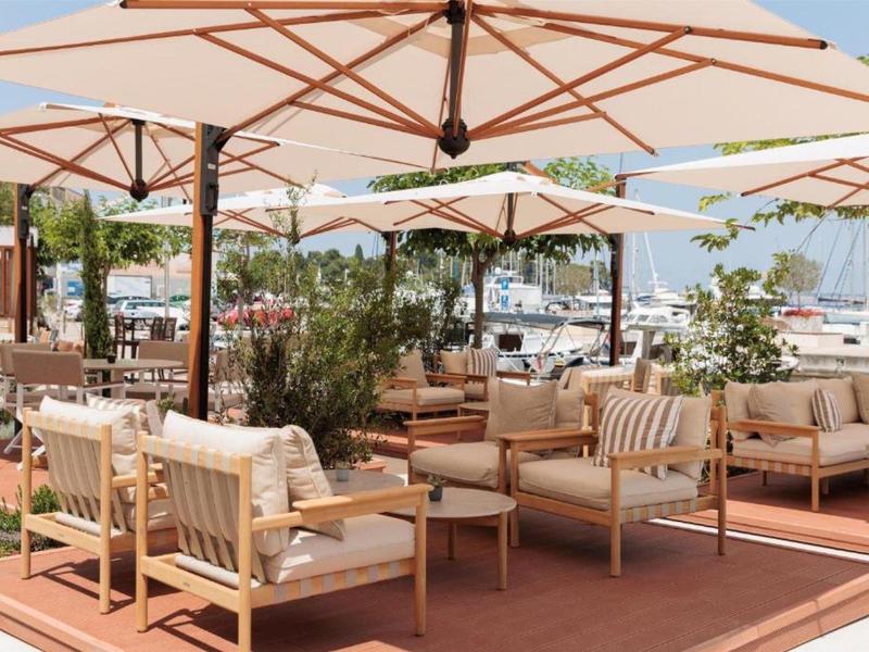 Terrasse extérieure confortable avec mobilier en bois et parasols près d'un port calme.