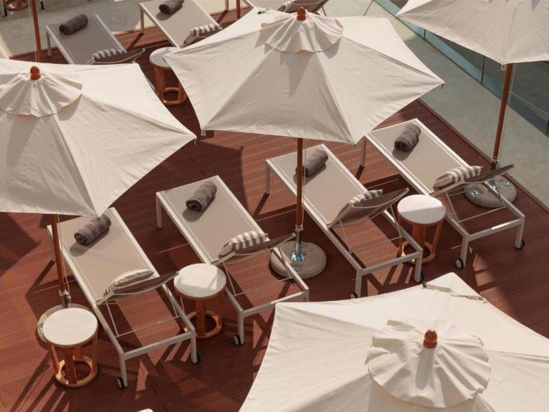 Plusieurs chaises longues avec parasols blancs sur une terrasse à côté d'une piscine.