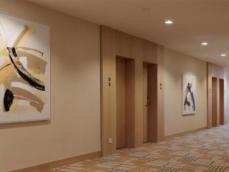 Couloir d'hôtel avec ascenseurs, peintures abstraites modernes et sol en moquette.