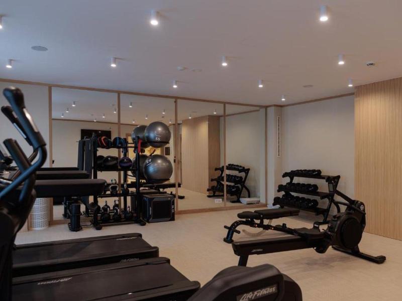 Salle de sport moderne avec tapis de course et haltères devant de grands miroirs et murs en bois.