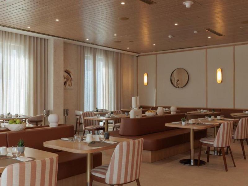 Salle de restaurant d'hôtel moderne avec tables, fauteuils et banquettes confortables.
