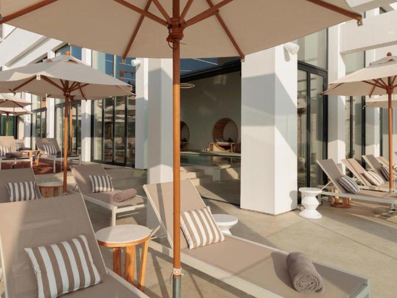 Terrasse d'hôtel ensoleillée avec chaises longues, parasols et espaces de détente confortables.