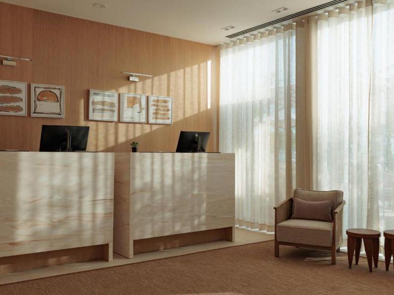 Espace de réception lumineux avec comptoir en bois, fauteuil et grandes fenêtres avec rideaux.