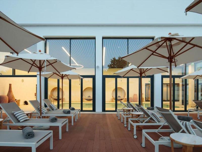 Terrasse ensoleillée moderne avec chaises longues et parasols devant un bâtiment hôtelier.
