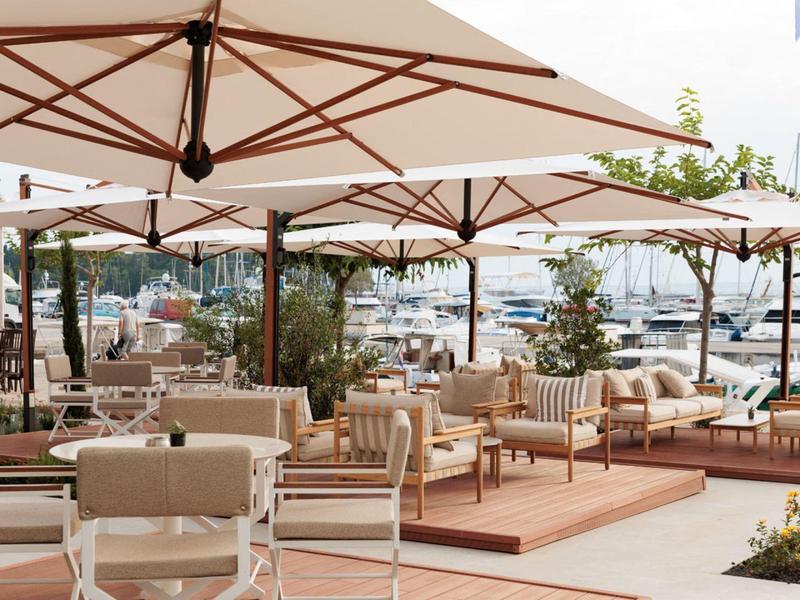 Terrasse avec des chaises confortables et des parasols avec vue sur des yachts dans le port